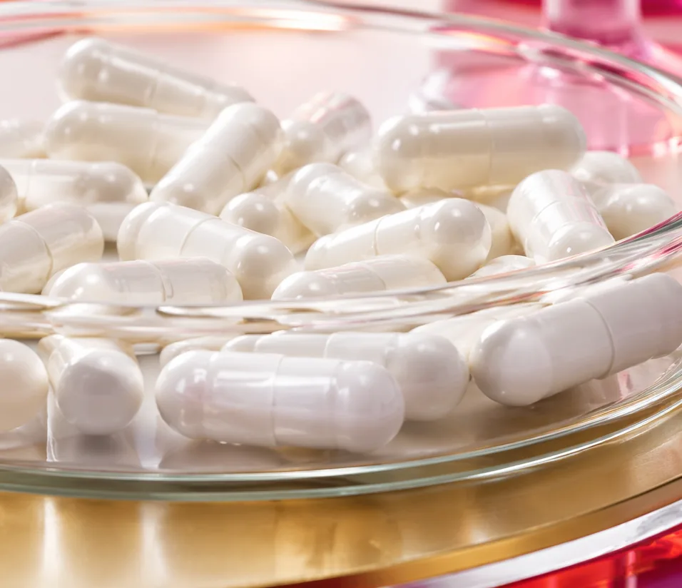 White hard capsules in a glass dish, the finished format of many digestive enzyme blends